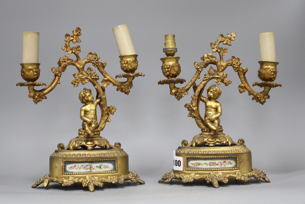 A pair of French gilt metal two light candelabra, modelled with putti seated beneath vine branches and inset with Sevres style